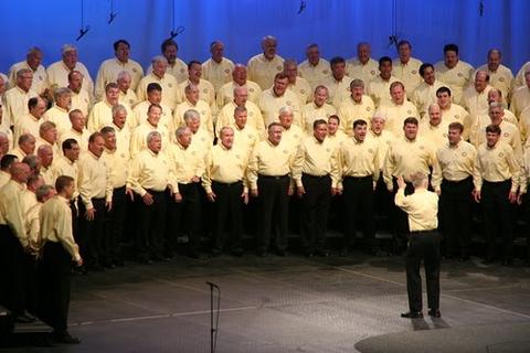 A cropped photo of a harmony brigade chorus all in yellow shirts and black slacks.